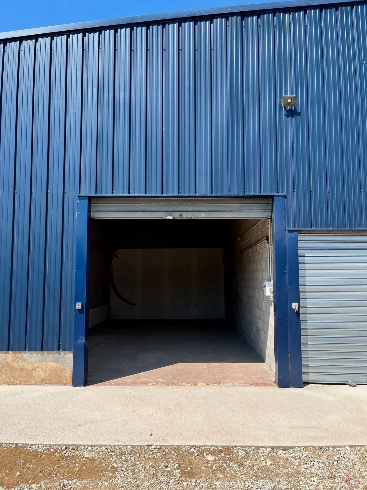 La porte du local A1 ouverte, sur la façade bleue de l’entrepôt