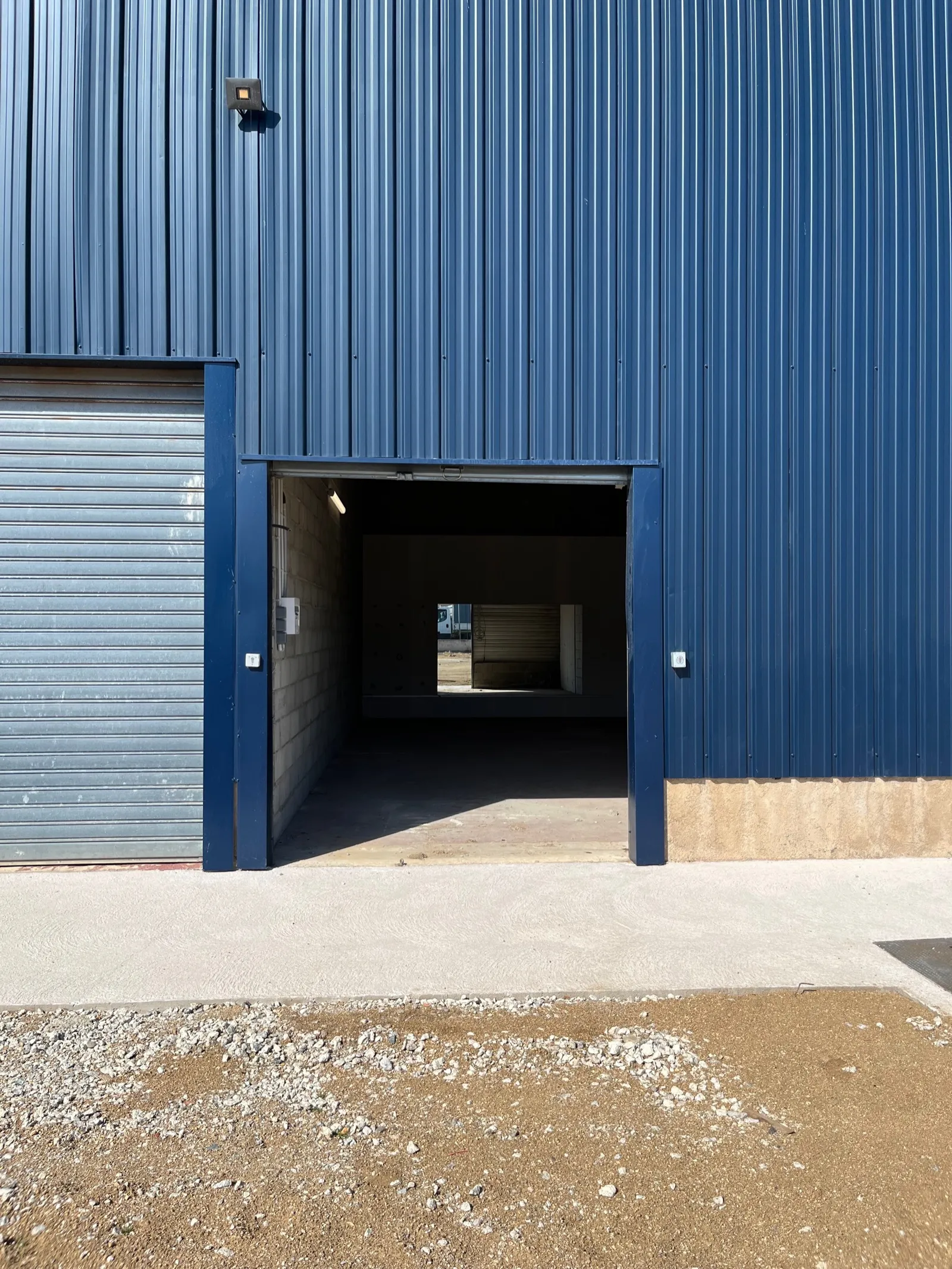 L’entrée du local A2, grande porte ouverte sur la façade bleue de l’entrepôt