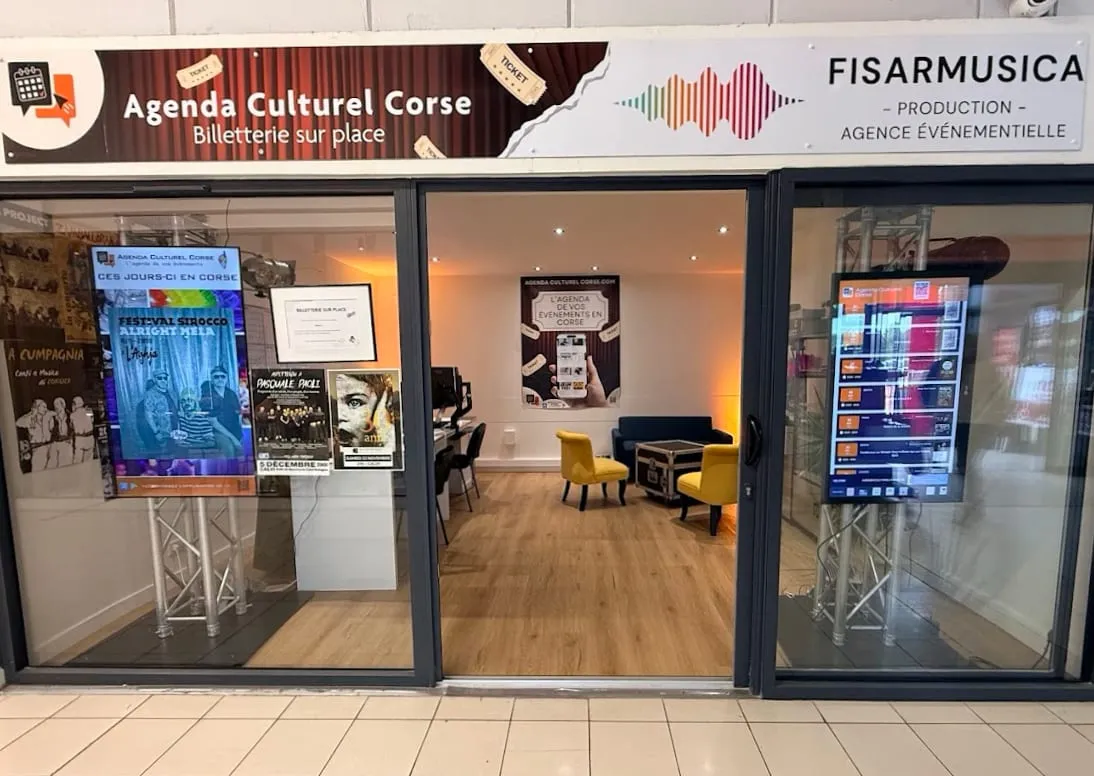 La vitrine de l'Agenda Culturel Corse dans la galerie : son enseigne « Billetterie sur place », ses affiches de spectacles et son écran tactile