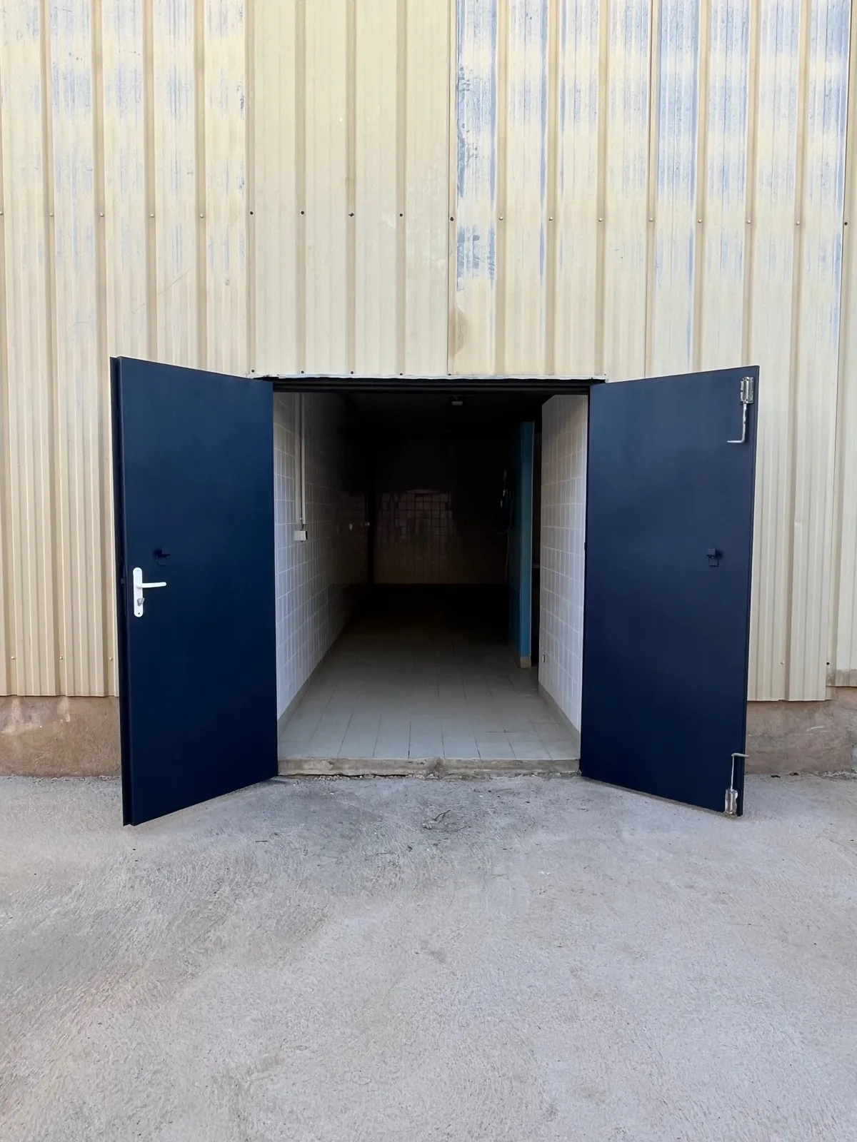 La porte métallique à deux battants du local C1, ouverte sur la façade de l’entrepôt