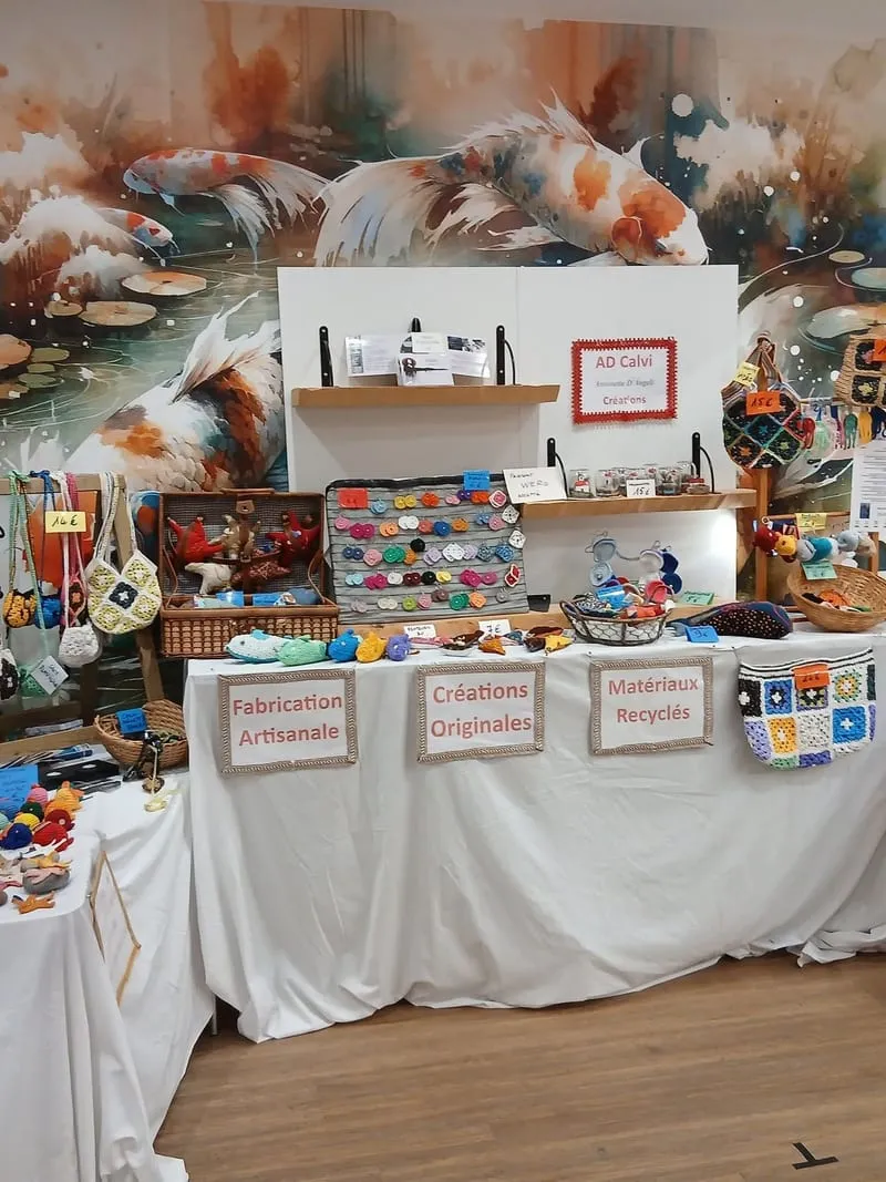 Le stand AD Calvi Créations : sacs, pochettes et petits personnages au crochet, sous les pancartes « Fabrication artisanale », « Créations originales » et « Matériaux recyclés »