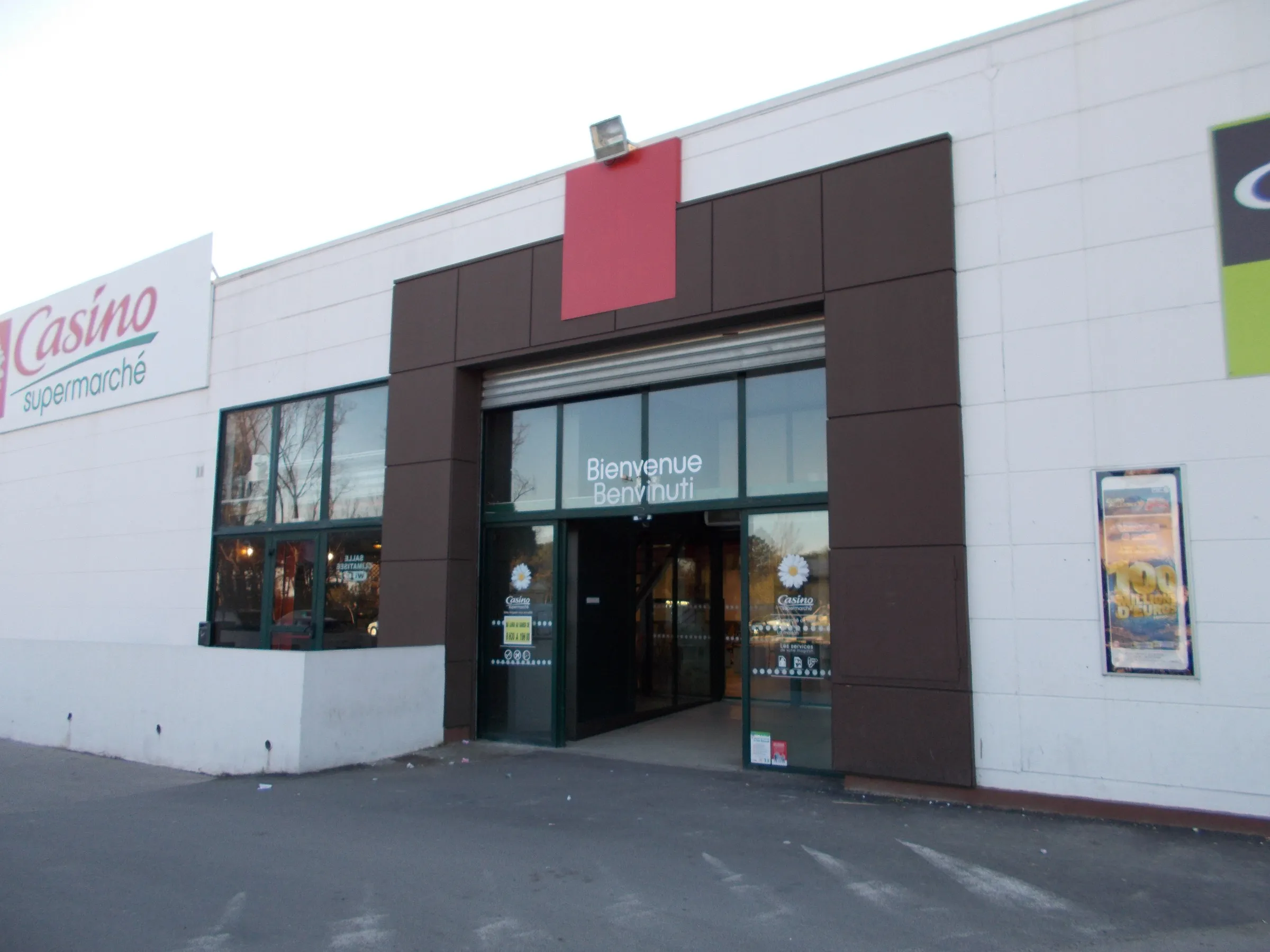Entrée vitrée du supermarché Casino avec l'inscription « Bienvenue – Benvinuti »