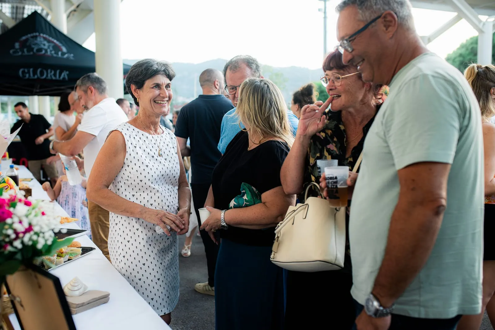 Des invités échangent, un verre à la main, près du buffet fleuri