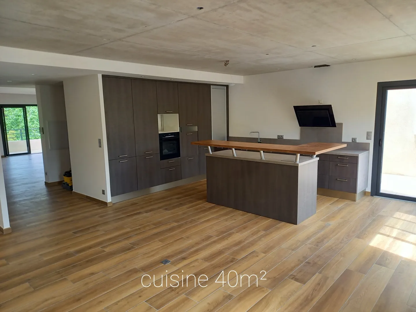 La cuisine de 40 m² : grands placards, four encastré, îlot central avec comptoir en bois