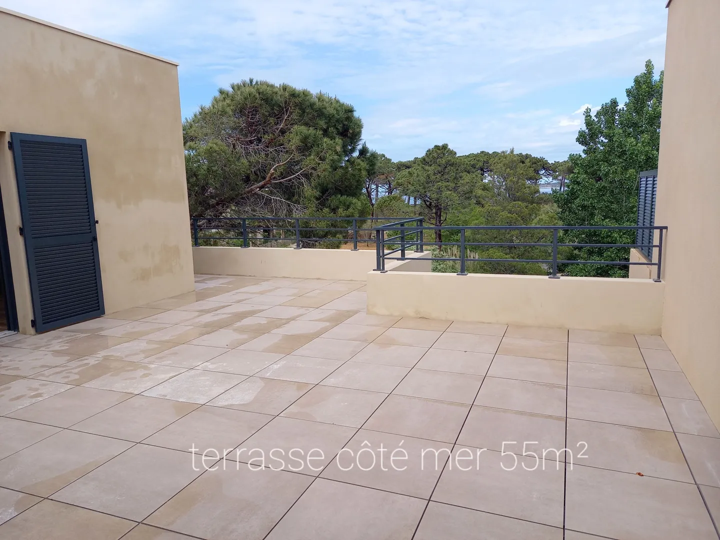 La terrasse côté mer de 55 m², carrelée, entourée de pins