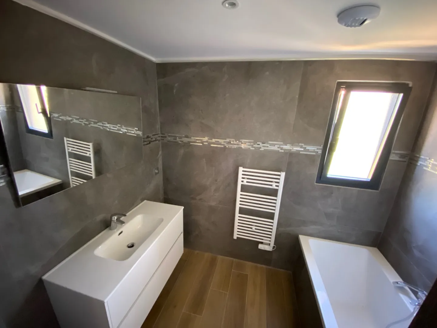 La salle de bain : meuble vasque, grand miroir, sèche-serviettes et baignoire