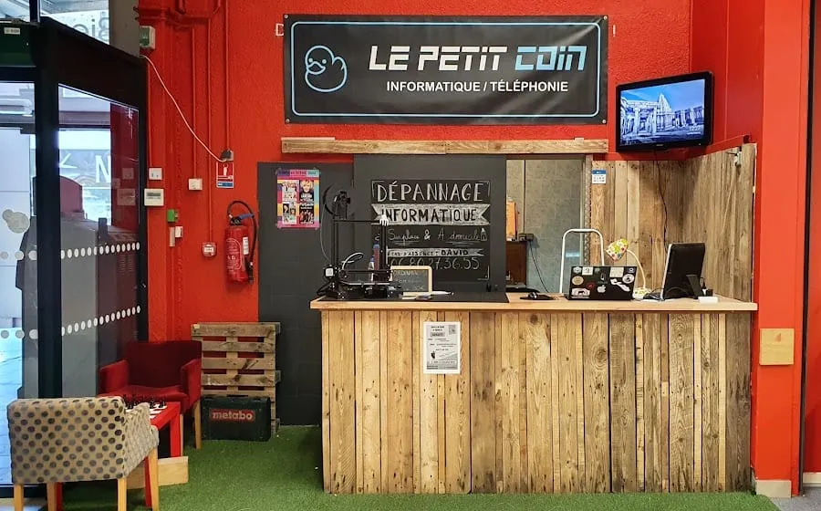 Le comptoir du Petit Coin dans la galerie : son enseigne, son ardoise « Dépannage informatique » et le matériel en réparation
