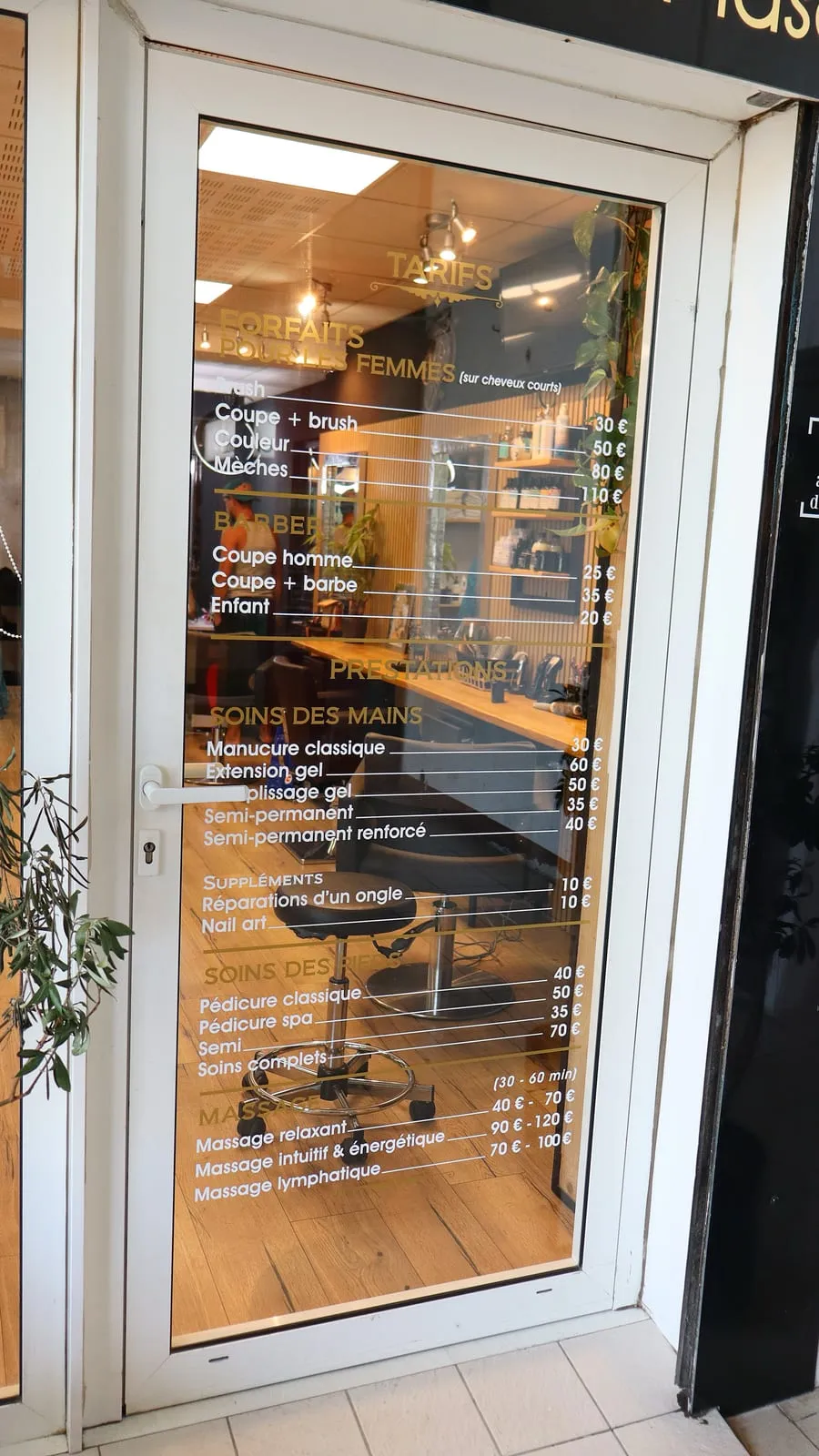 La porte du salon Nuance et ses tarifs affichés sur la vitre : coiffure, barbier, soins des mains et des pieds, massages