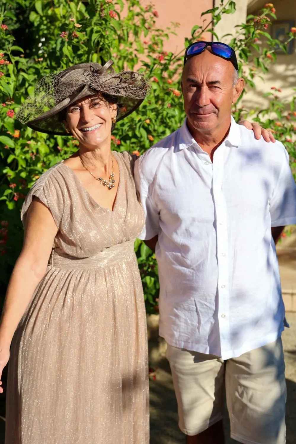 Vanina et Ranca côte à côte dans un jardin fleuri, elle en robe dorée et chapeau, lui en chemise blanche