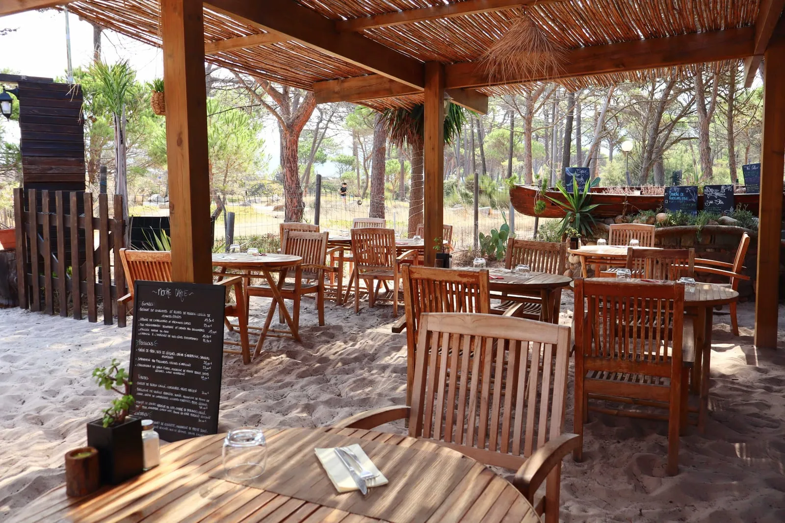 La terrasse du restaurant Vol Õ Vents sous sa pergola de roseaux, ses tables sur le sable et la pinède de Calvi